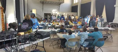 Grande salle avec de longues tables, du matériel de sonorisation et des invités qui s'installent.