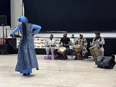 Une danseuse en robe bleue à motifs au premier plan, les percussionnistes derrière elle.