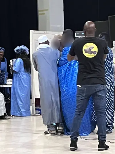 Des invités en tenues bleues debout, un homme en tee-shirt noir vu de dos au premier plan.