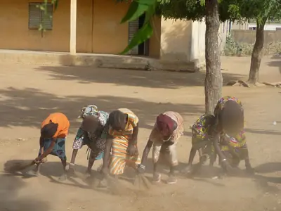 Des enfants balaient la cour de l'école.